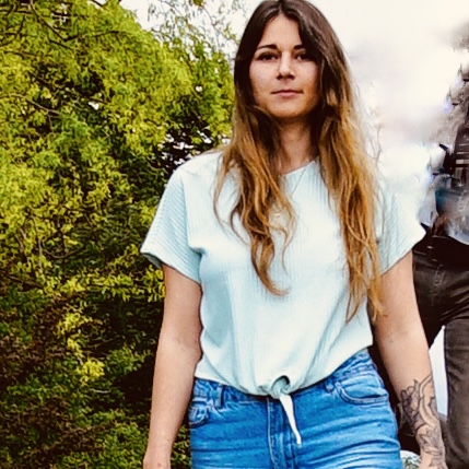 Eine junge Frau schaut in die Ferne, läuft draußen in blauem T-Shirt wie ein Model zur Kamera, Evi Heinrich