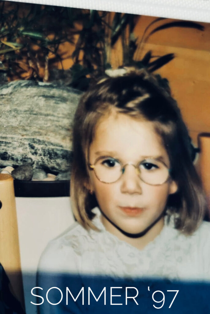 Ein kleines Mädchen schaut in die Kamera auf einem Privatbild aus den 90ern. Unten steht "Sommer 97" im Bild.